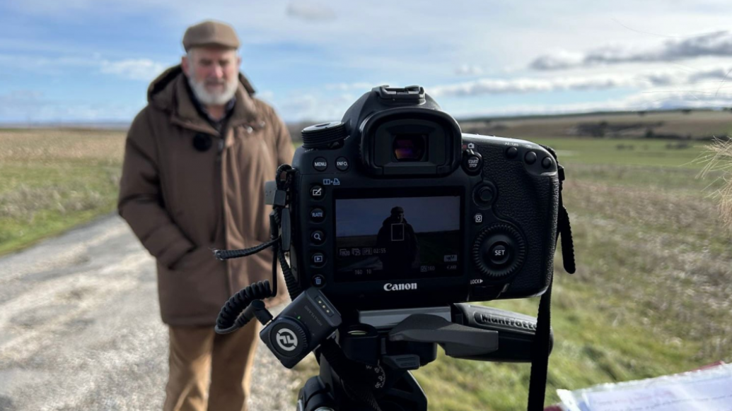 Cámara en primer plano grabando a un hombre en un paisaje rural de la España vaciada para un documental.