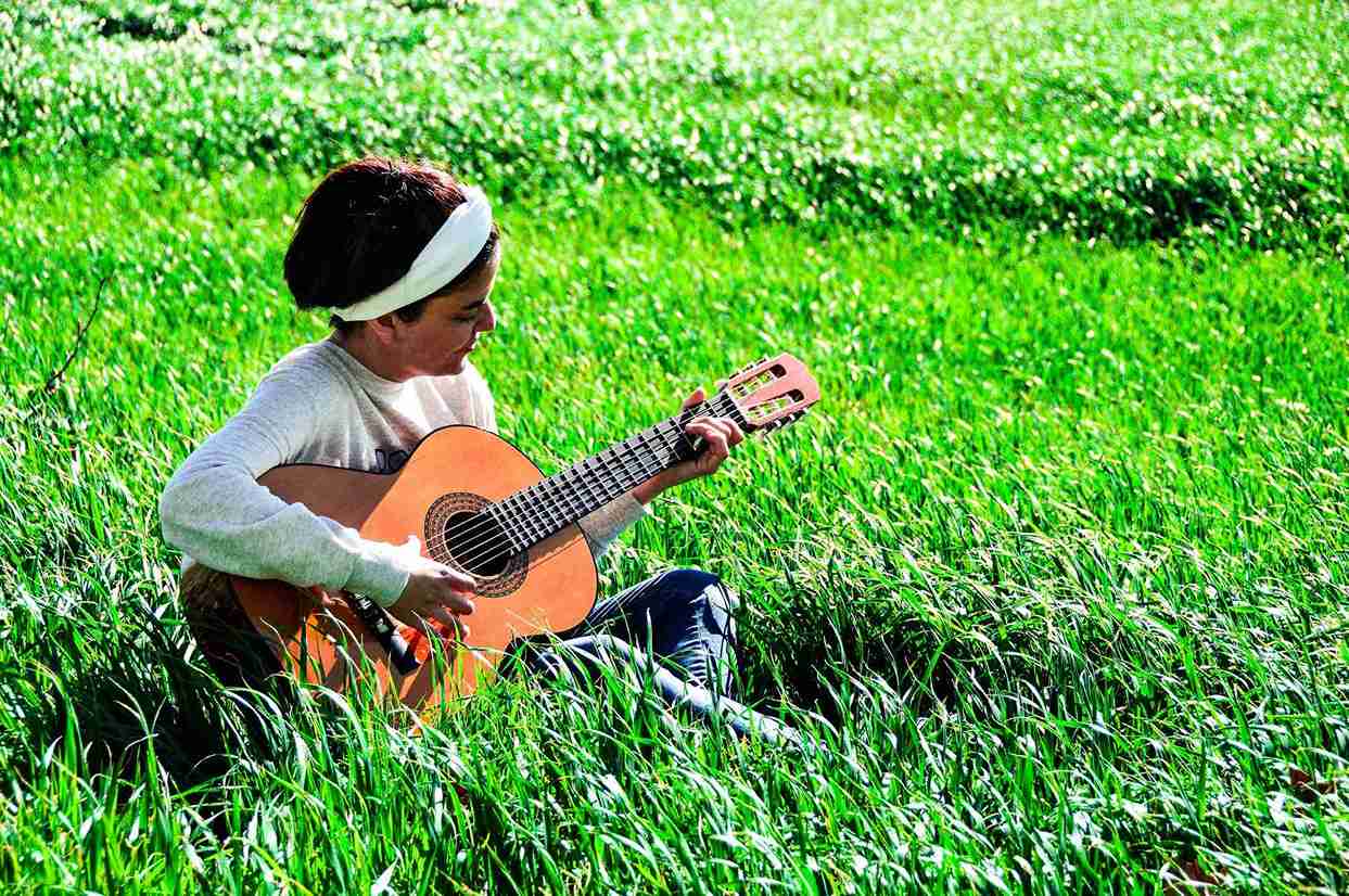Una mujer sentada en un campo verde tocando una guitarra acústica.