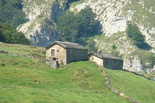 Cabaña pasiega enclavada en plena montaña cántabra, rodeada de prados verdes y formaciones rocosas calizas.