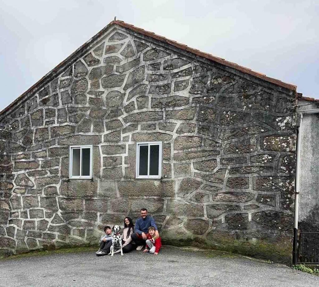 Aurora Matés con su familia y su perro dálmata, sentados frente a la fachada de piedra de su casa rural en una aldea de Ourense (Galicia).