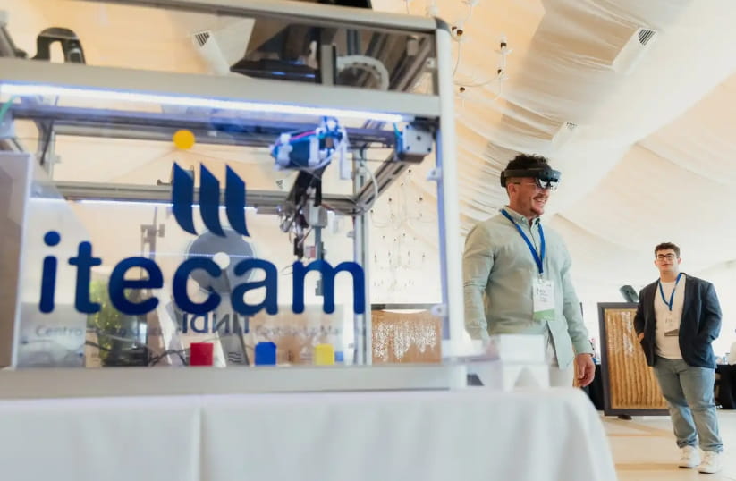 Impresora 3D y demostración de gafas de realidad aumentada en un stand de ITECAM, con el logo de ITECAM en primer plano.