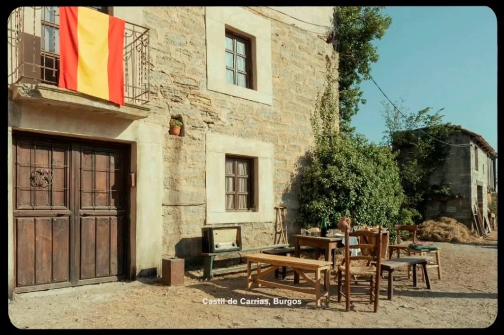 "Fachada de piedra con bandera española y mesas al aire libre en Castil de Carrias, Burgos, localización de La bola negra"