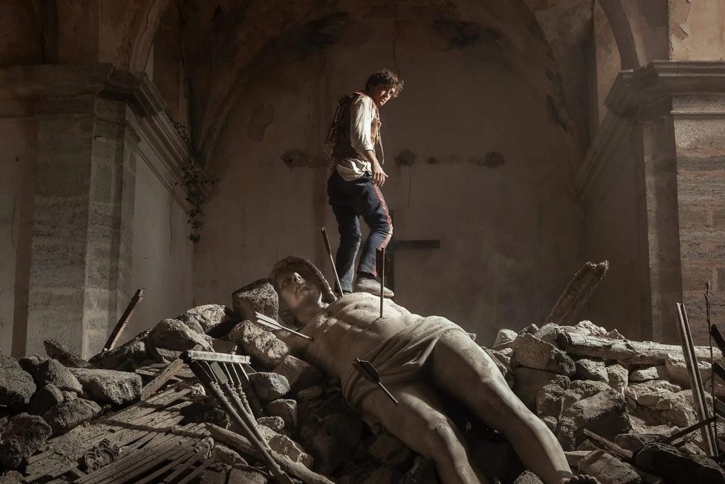 Fotograma de La bola negra: un joven soldado sobre los escombros de una iglesia bombardeada junto a una estatua derribada
